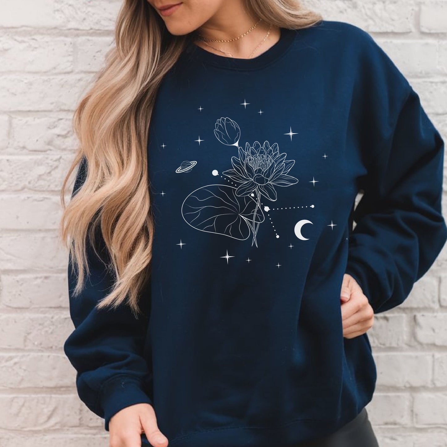 Person wearing a navy blue sweatshirt with celestial design against a light brick wall.
