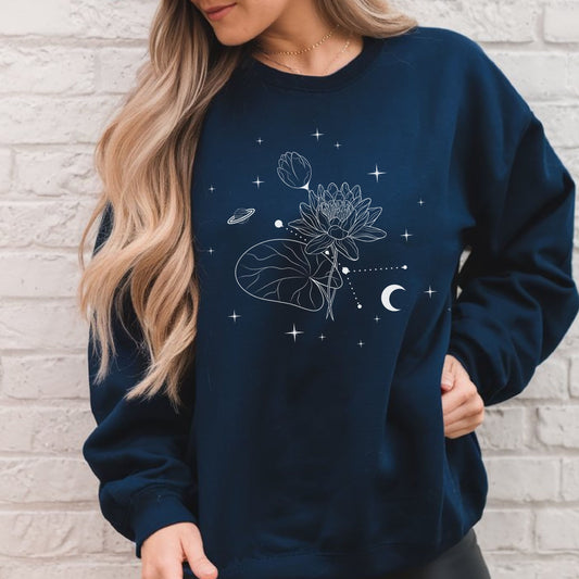 Person wearing a navy blue sweatshirt with celestial design against a light brick wall.