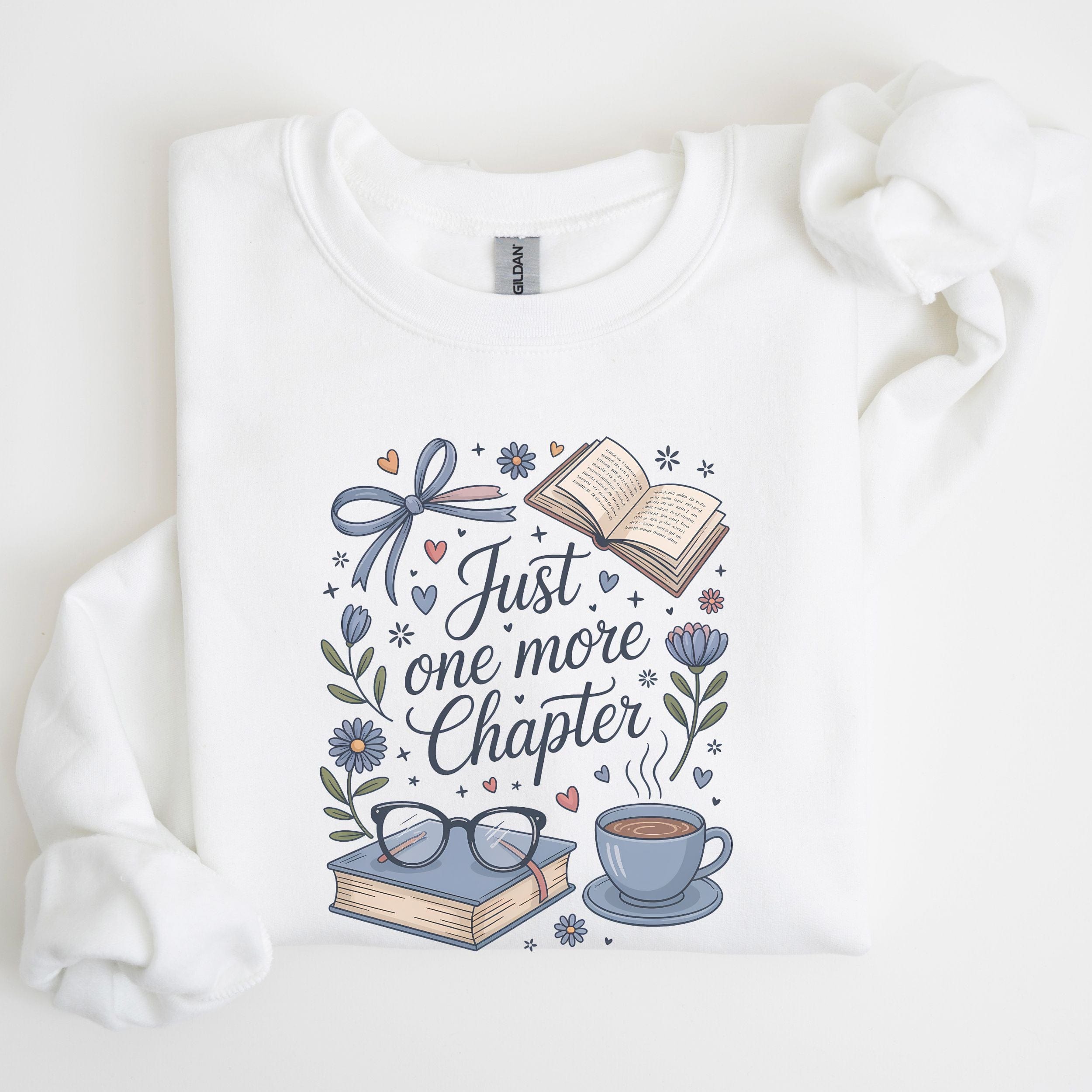 White sweatshirt with 'Just one more chapter' design featuring books, a cup, and glasses on a white background.