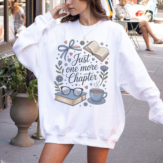 Person wearing a white sweatshirt with a book-themed design and text outdoors.
