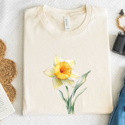 Beige t-shirt with a yellow flower design on a light gray surface.