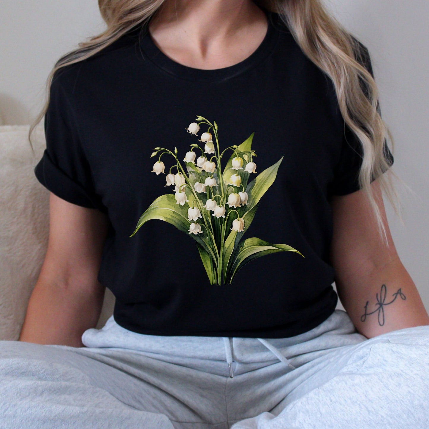 Person wearing a black t-shirt with a floral design, sitting on a couch.