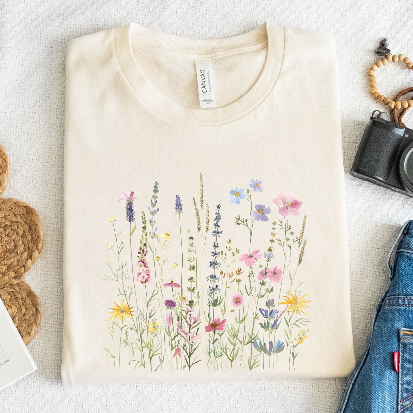 Beige t-shirt with floral design on a textured surface with accessories.