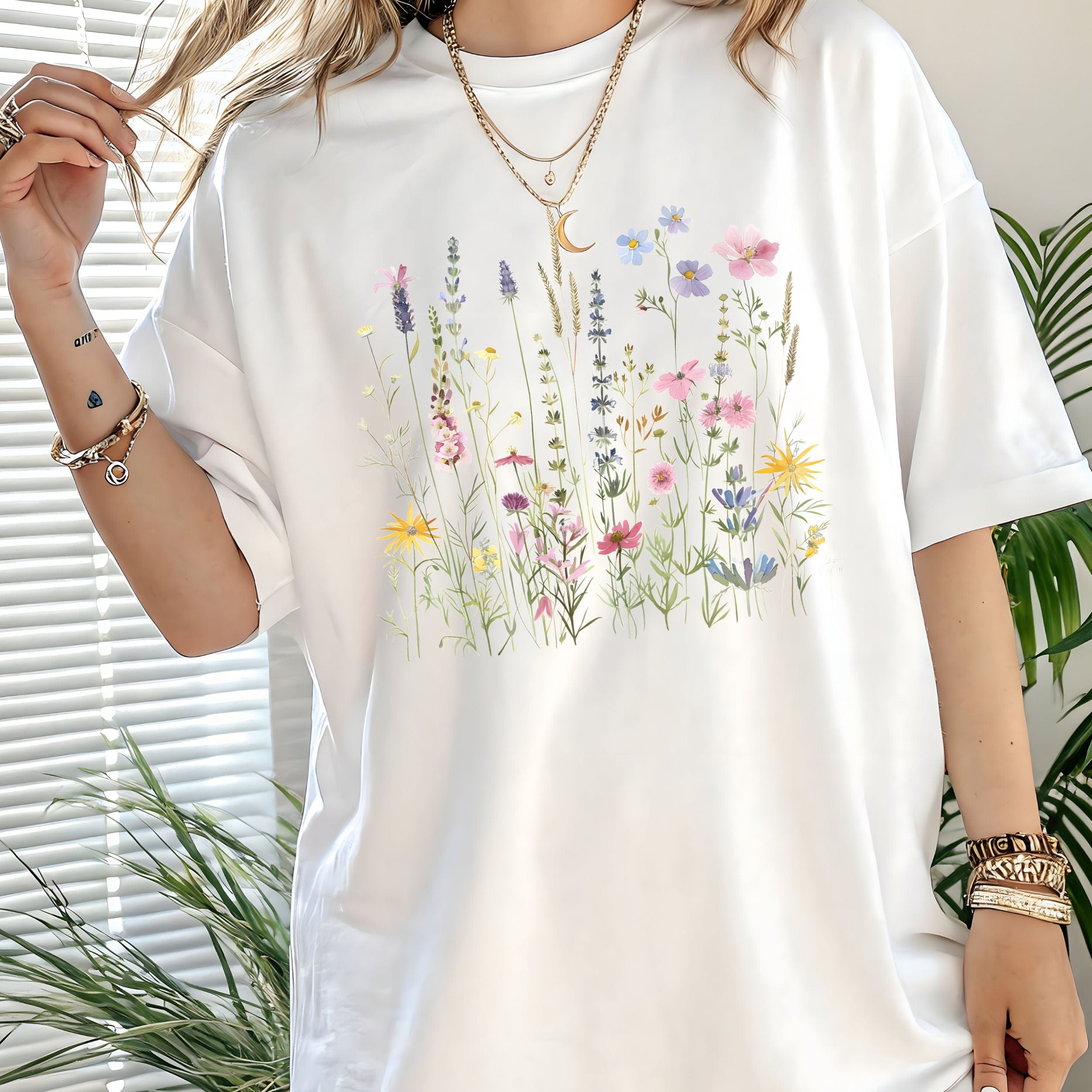 White t-shirt with floral design worn by a person, with plants in the background