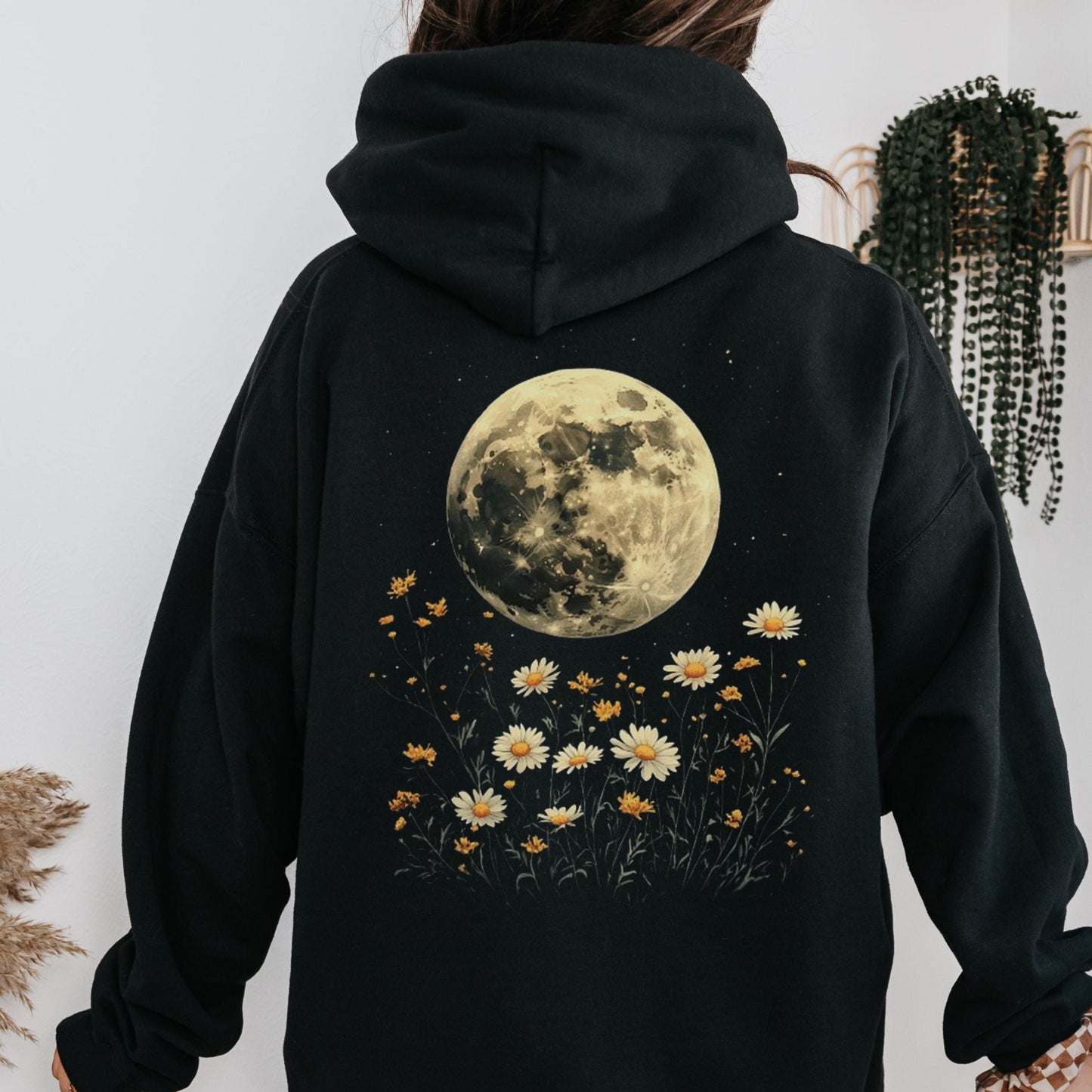 Black hoodie with a moon and floral design on the back, worn by a person.