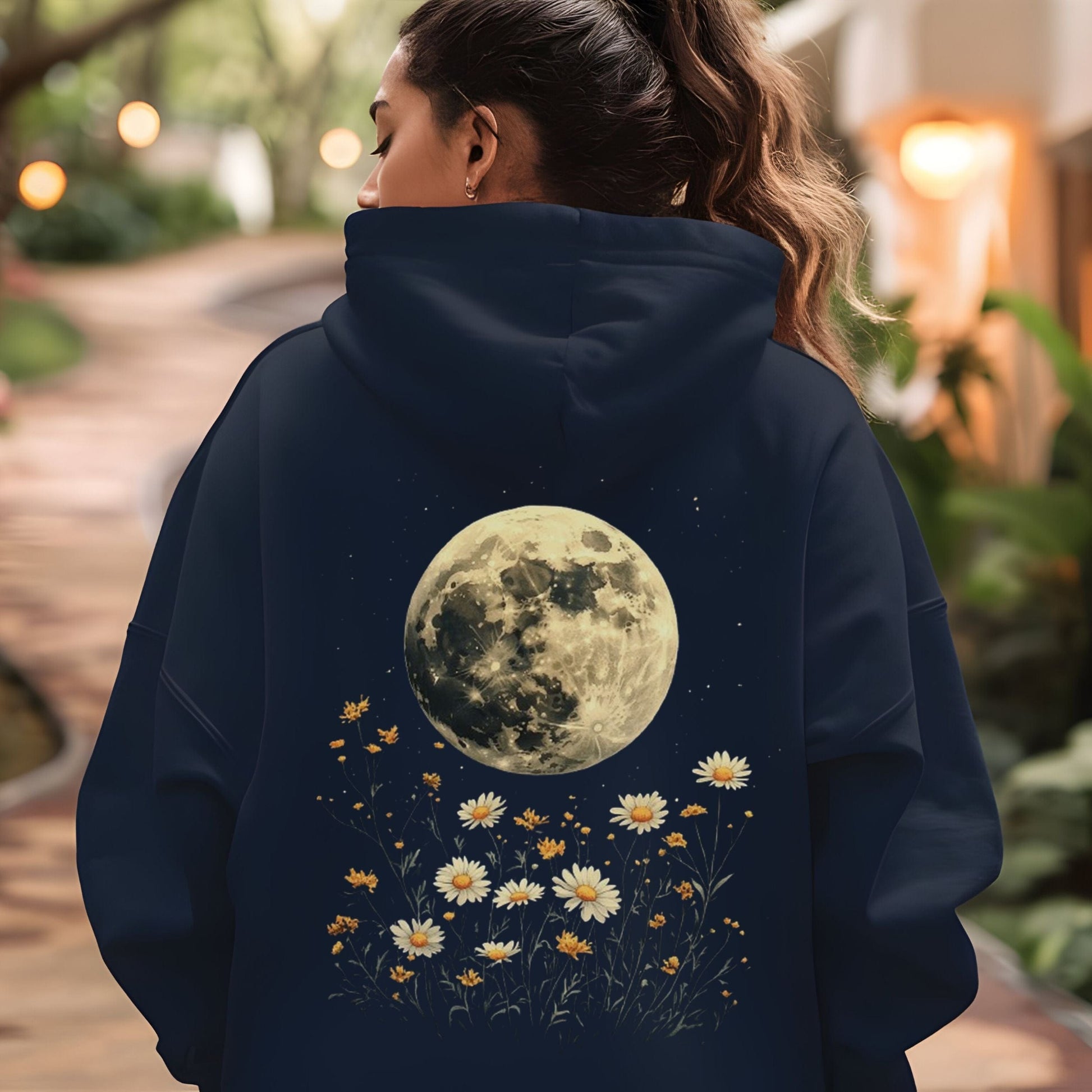 Person wearing a navy hoodie with a moon and floral design, standing outdoors.