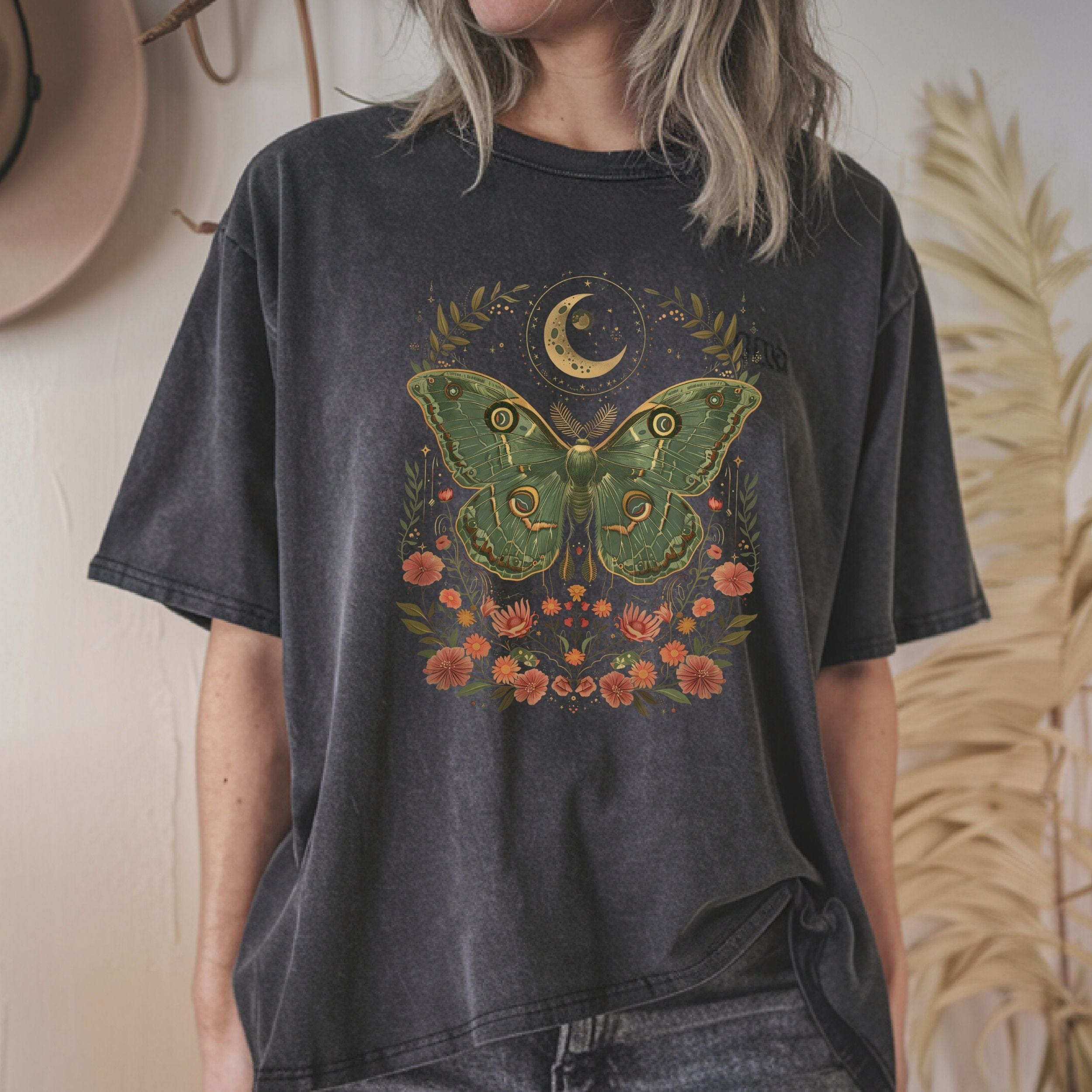 Person wearing a dark heather grey t-shirt with a green moth design against a neutral background