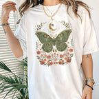White t-shirt with a green moth and floral design worn by a person.