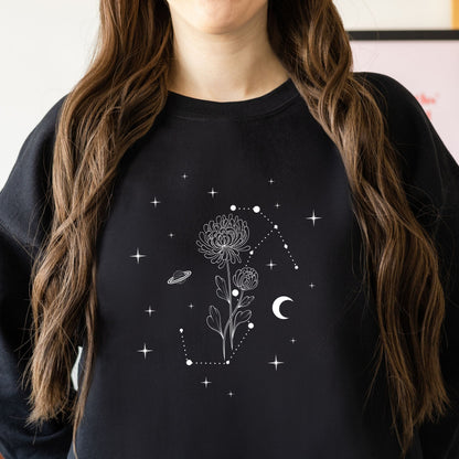Person wearing a black sweatshirt with celestial design featuring flowers, stars, and planets.
