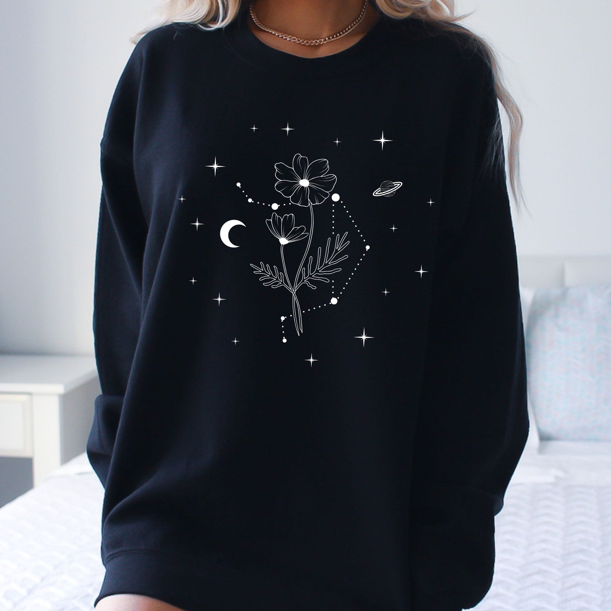 Black sweatshirt with floral and celestial design worn by a person.