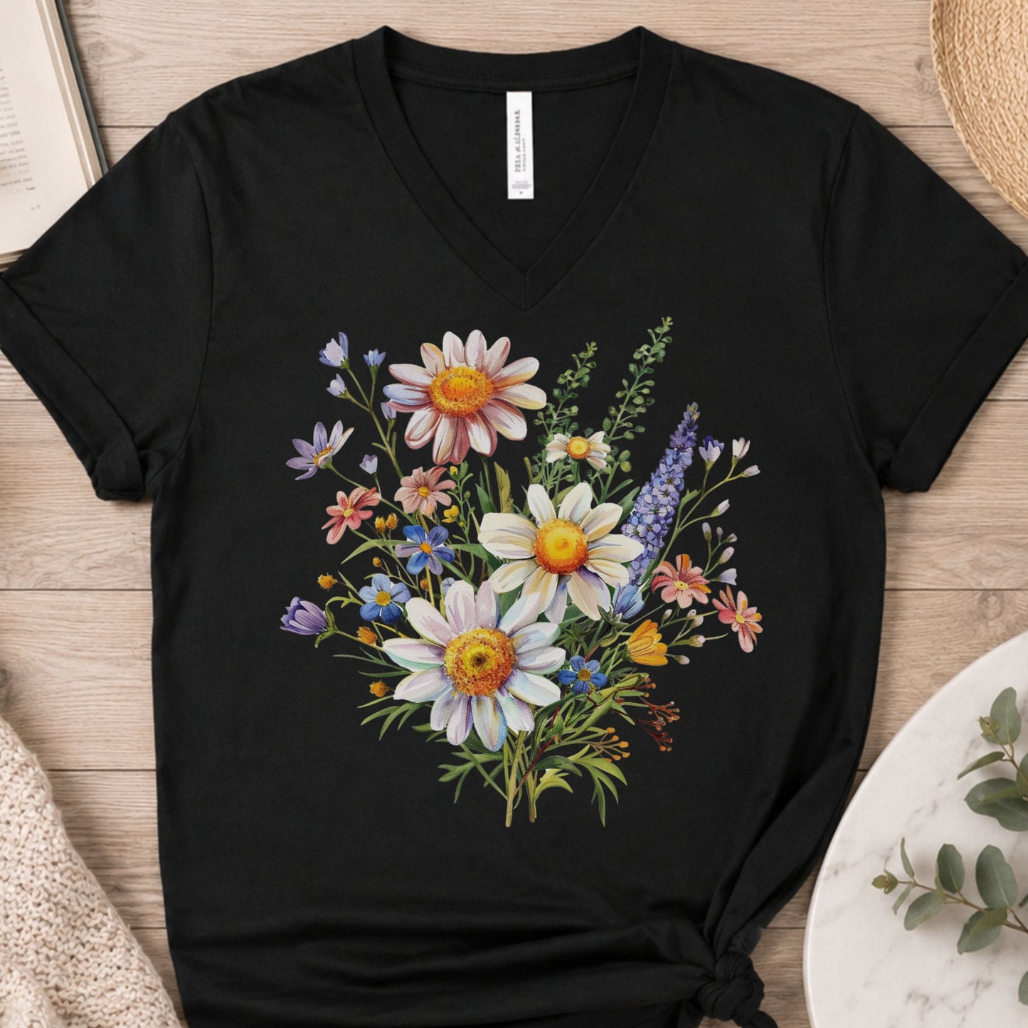 A black V-neck t-shirt with a colorful wildflower graphic print, laid flat on a light wood background.