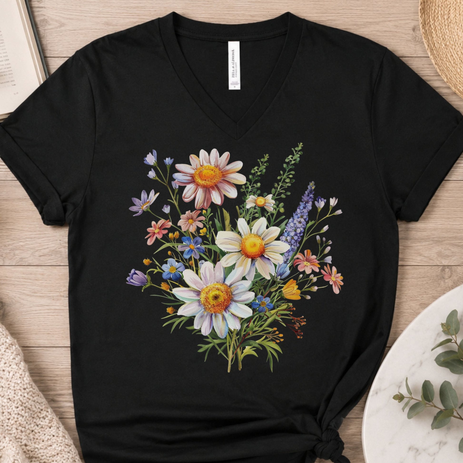 A black V-neck t-shirt with a colorful wildflower graphic print, laid flat on a light wood background.