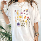 White t-shirt with floral design worn by a person, with a plant in the background.