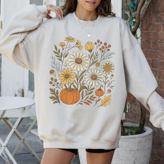 Person wearing a cream-colored sweatshirt with floral and pumpkin design outdoors.