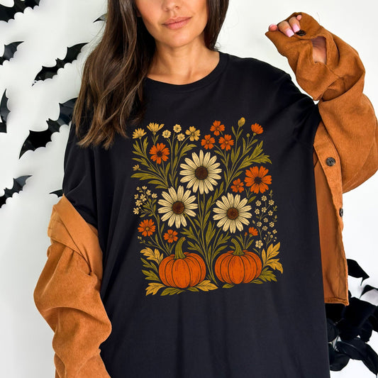 Person wearing a black t-shirt with floral and pumpkin design, surrounded by Halloween decorations.