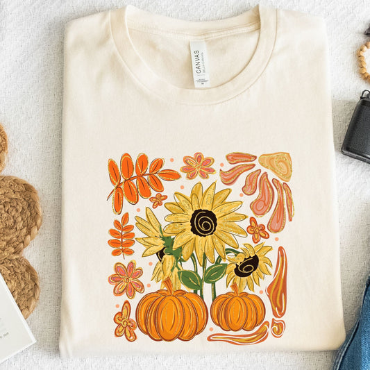 White t-shirt with autumn-themed design featuring sunflowers and pumpkins on a light background.