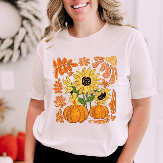 Person wearing a white t-shirt with autumn-themed design featuring pumpkins and sunflowers.