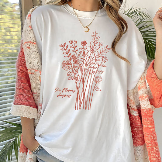 White t-shirt with floral design and text worn by a person, with plants in the background