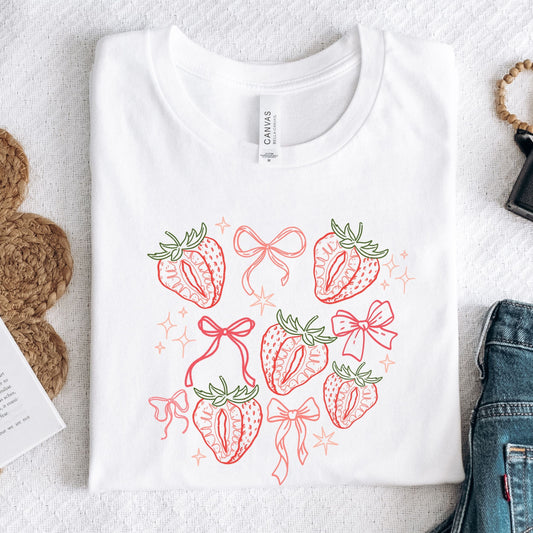White t-shirt with strawberry and bow design on a textured surface