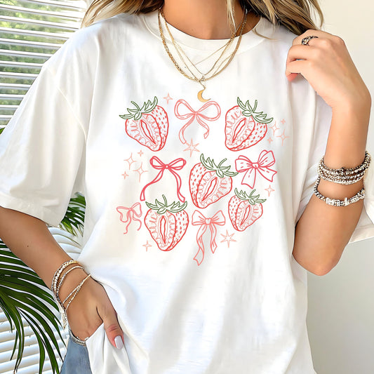 Person wearing a white t-shirt with strawberry and bow design, standing indoors.