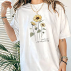 White t-shirt with sunflower design worn by a person, with a plant in the background.