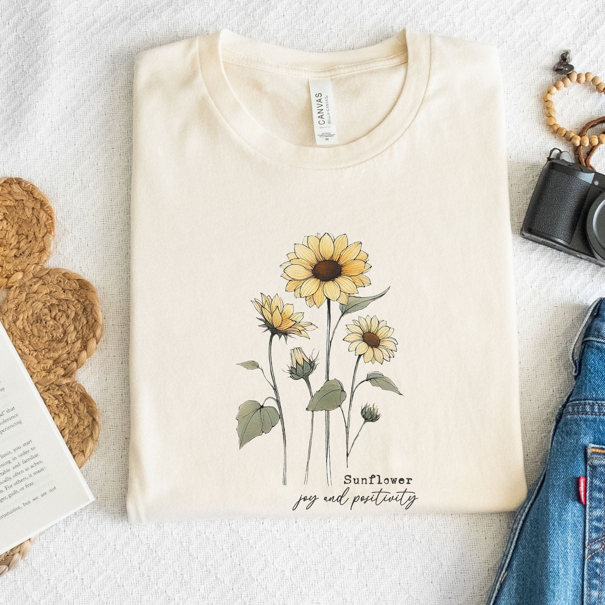 Beige t-shirt with sunflower design and text on a light surface with accessories.