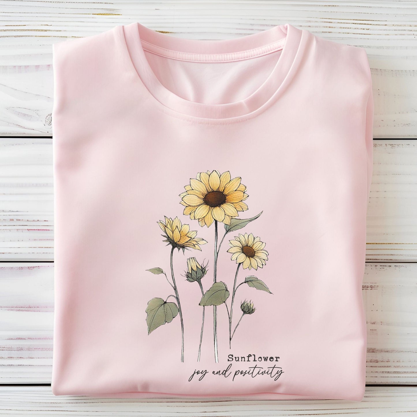 Soft pink t-shirt with sunflower design and text on a light gray surface.