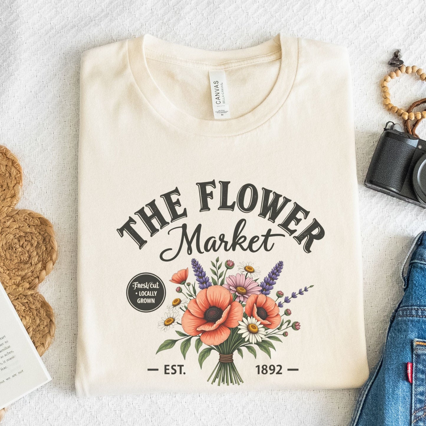 Beige t-shirt with 'The Flower Market' design on a textured surface.