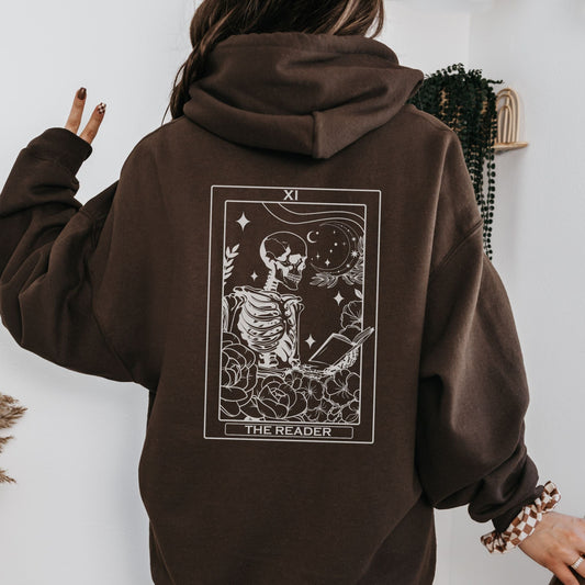 Person wearing a brown hoodie with a tarot card design on the back, against a white wall.