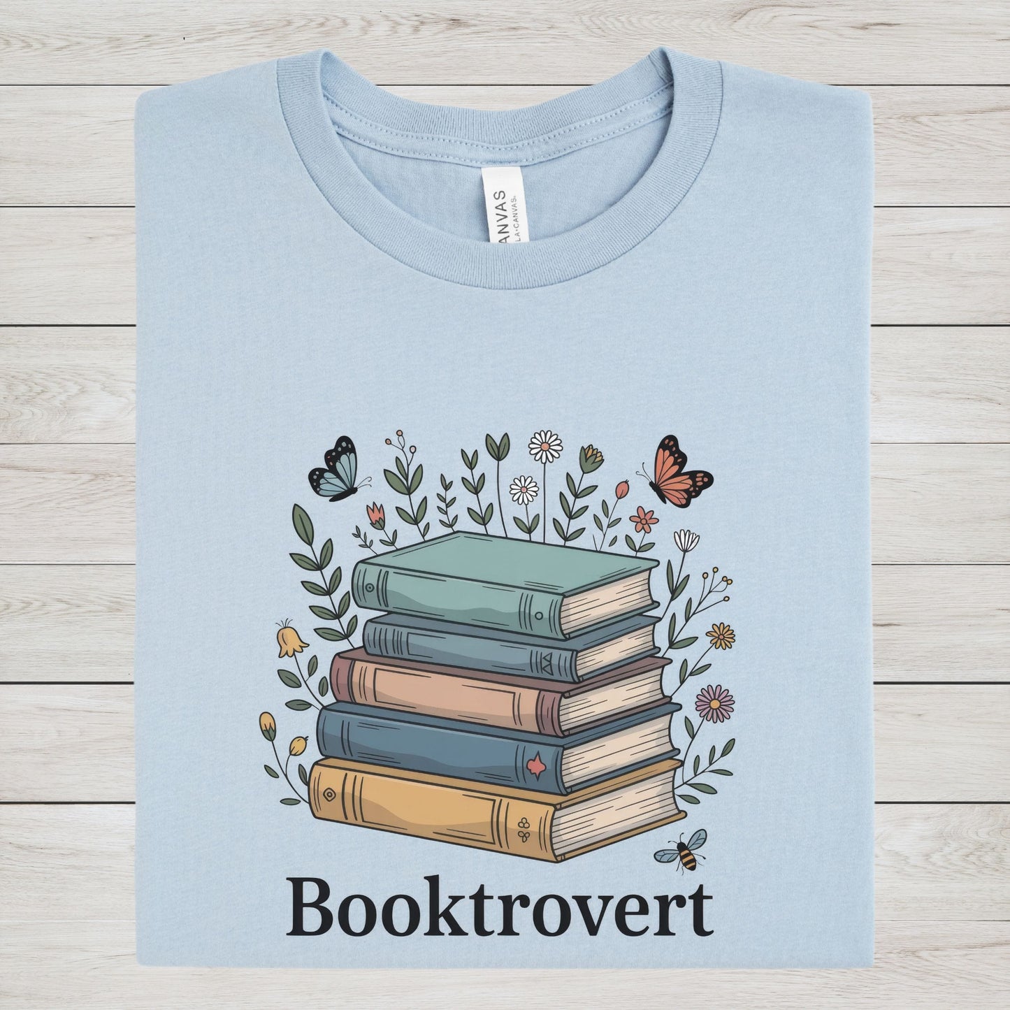 Light blue t-shirt with a graphic of books and flowers on a wooden surface