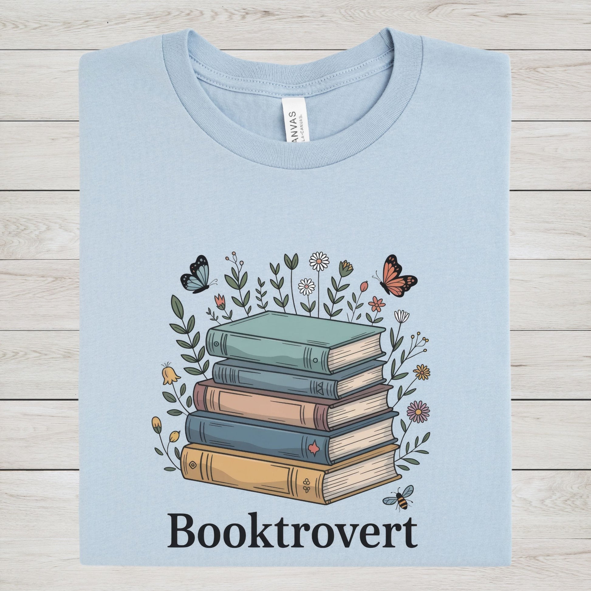 Light blue t-shirt with a graphic of books and flowers on a wooden surface