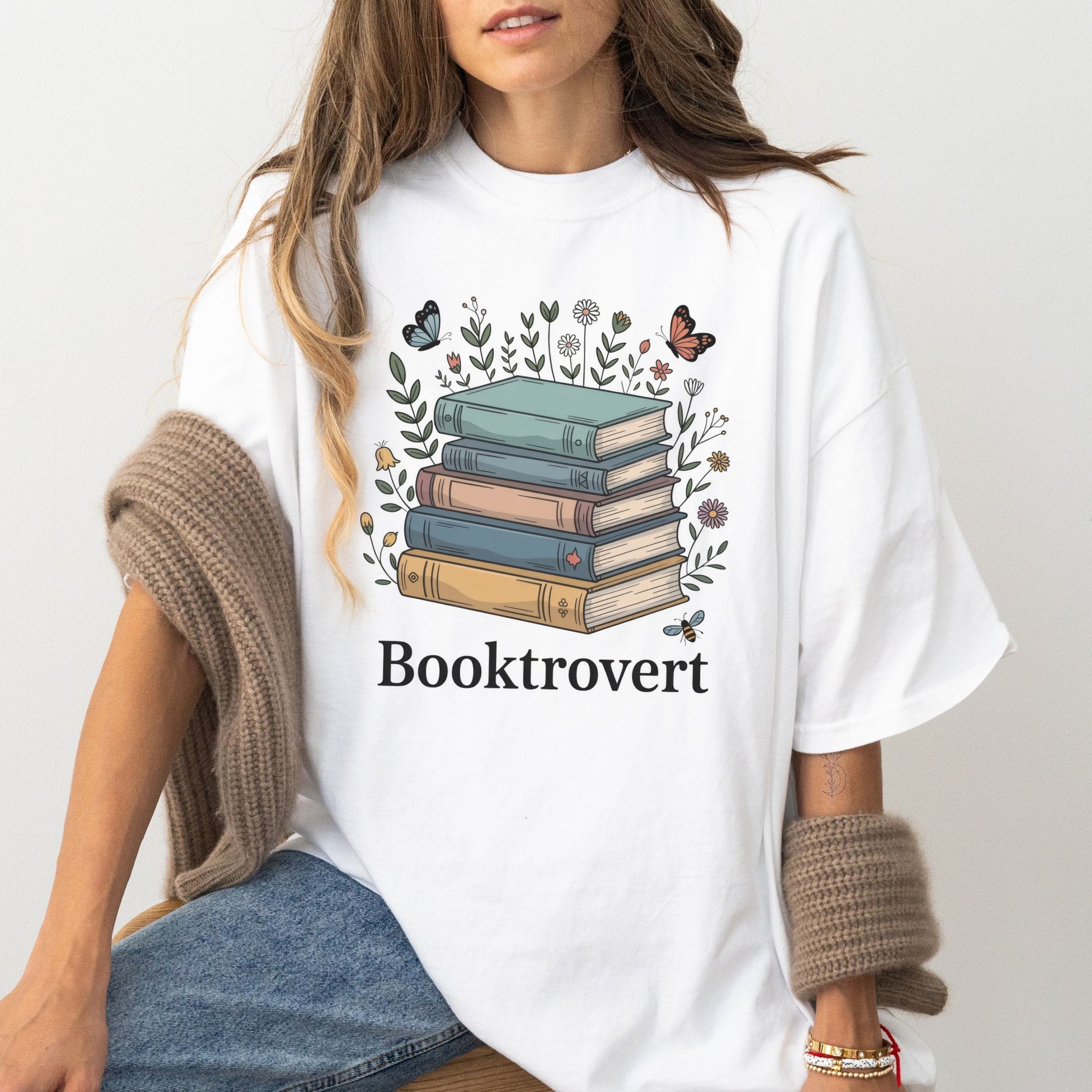 Person wearing a white t-shirt with a book-themed design and 'Booktrovert' text.