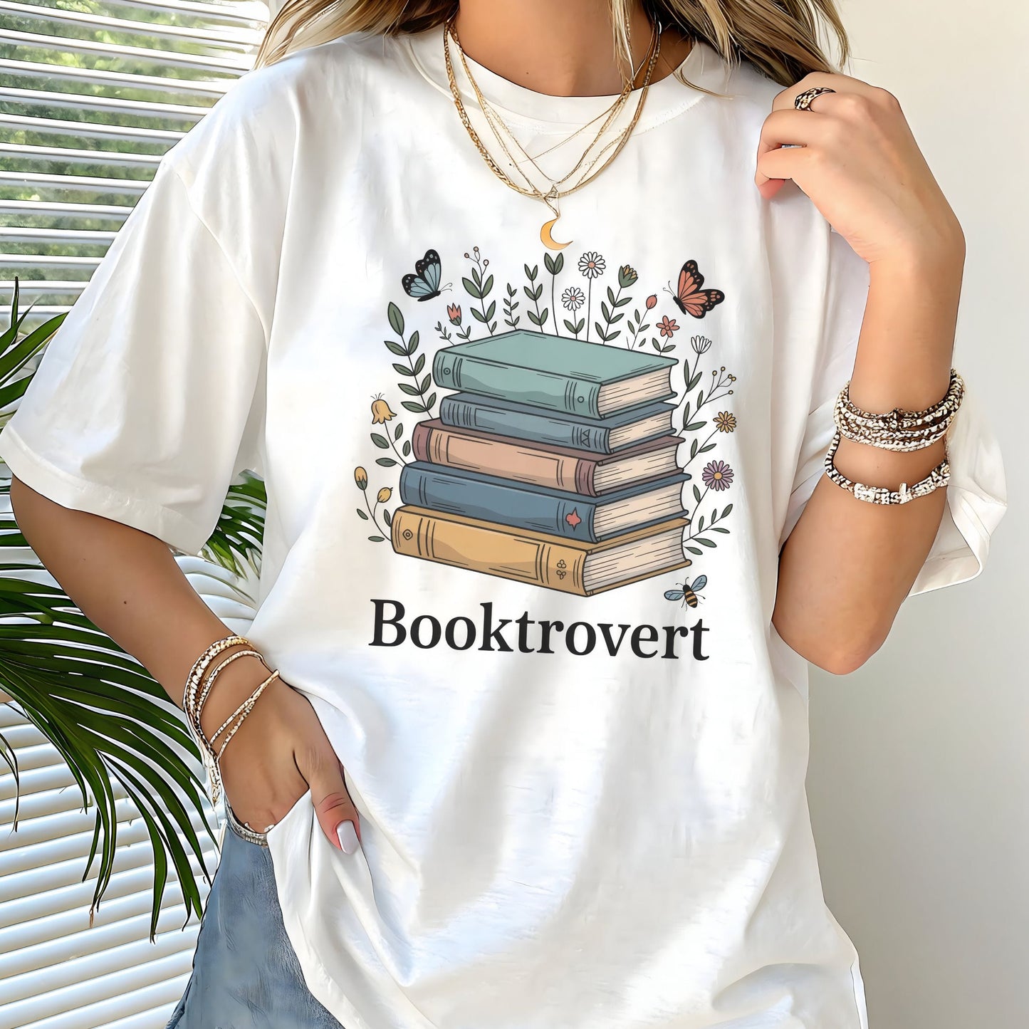 Person wearing a white t-shirt with a book-themed design and 'Booktrovert' text.