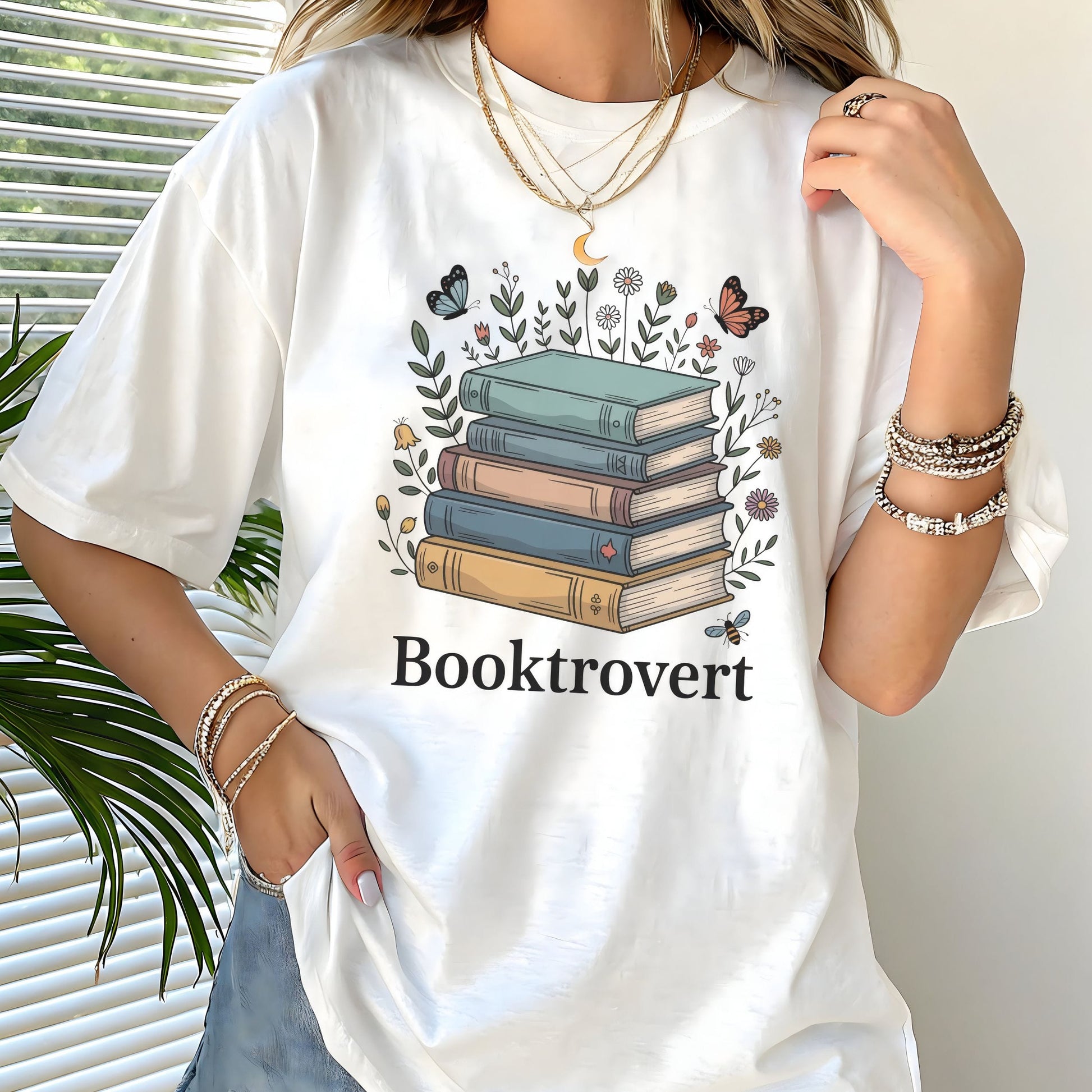 Person wearing a white t-shirt with a book-themed design and 'Booktrovert' text.
