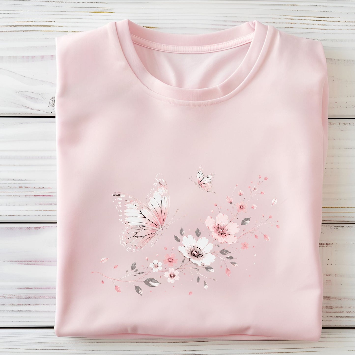 Folded pink t-shirt with floral and butterfly design on a wooden surface