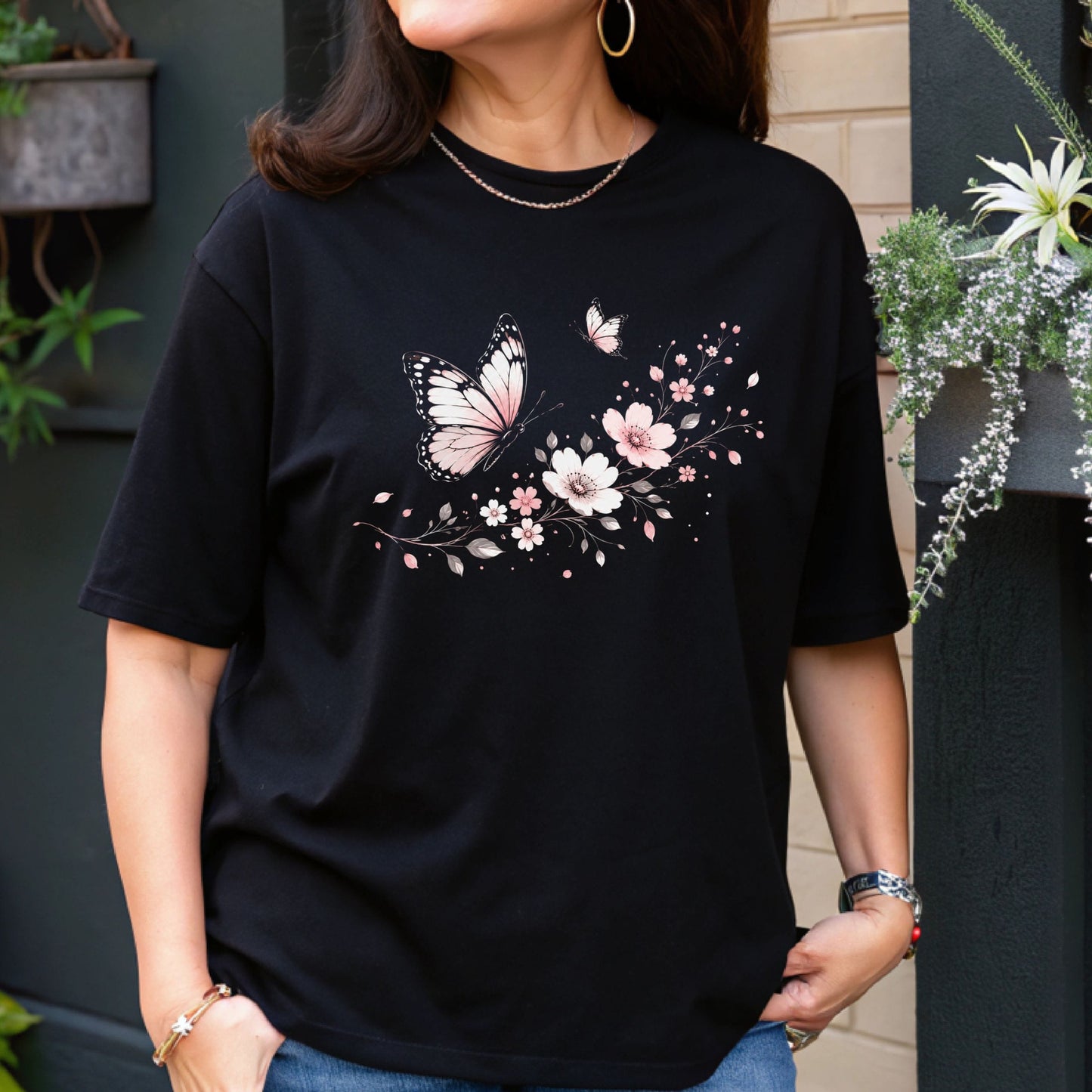 Person wearing a black t-shirt with butterfly and floral design outdoors.