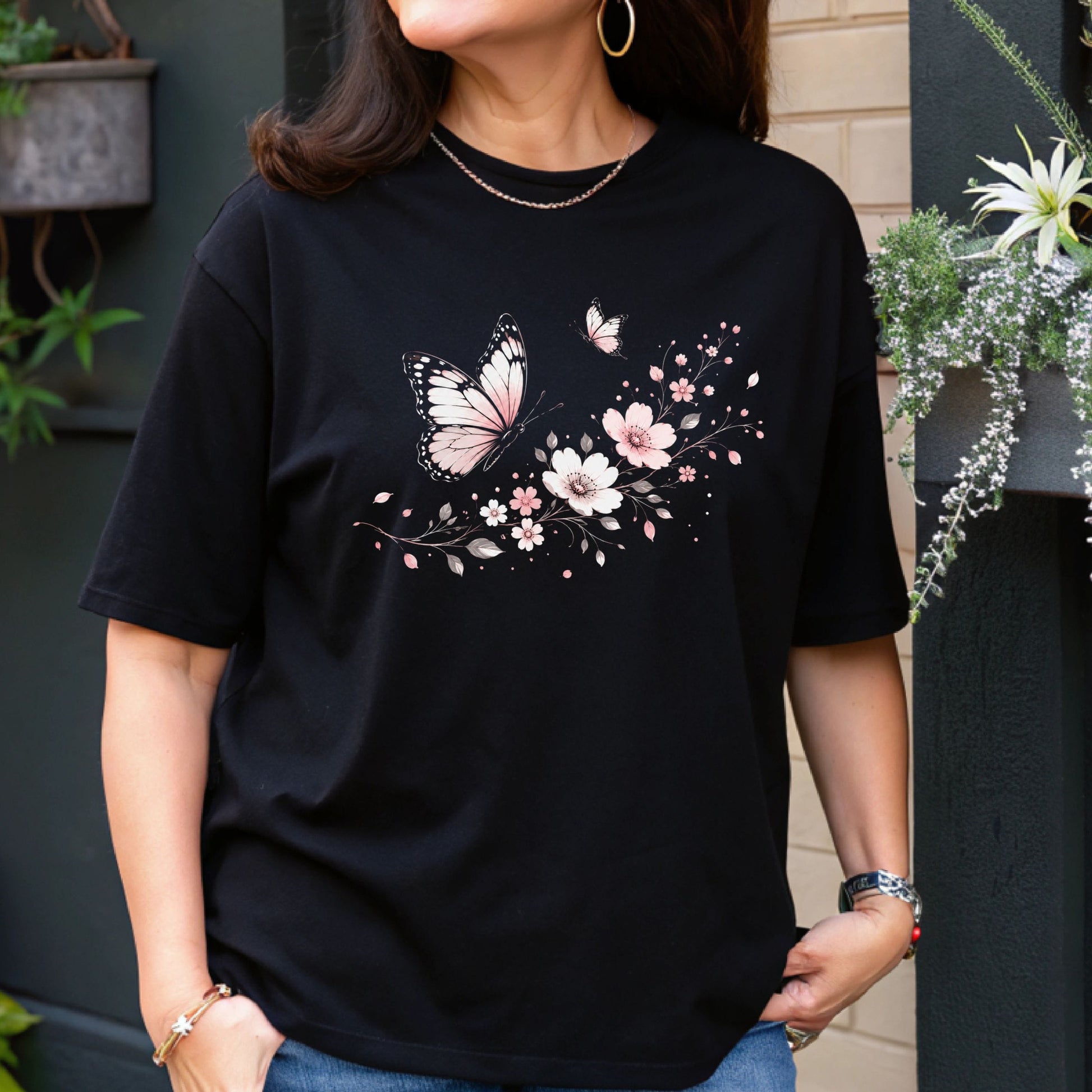 Person wearing a black t-shirt with butterfly and floral design outdoors.