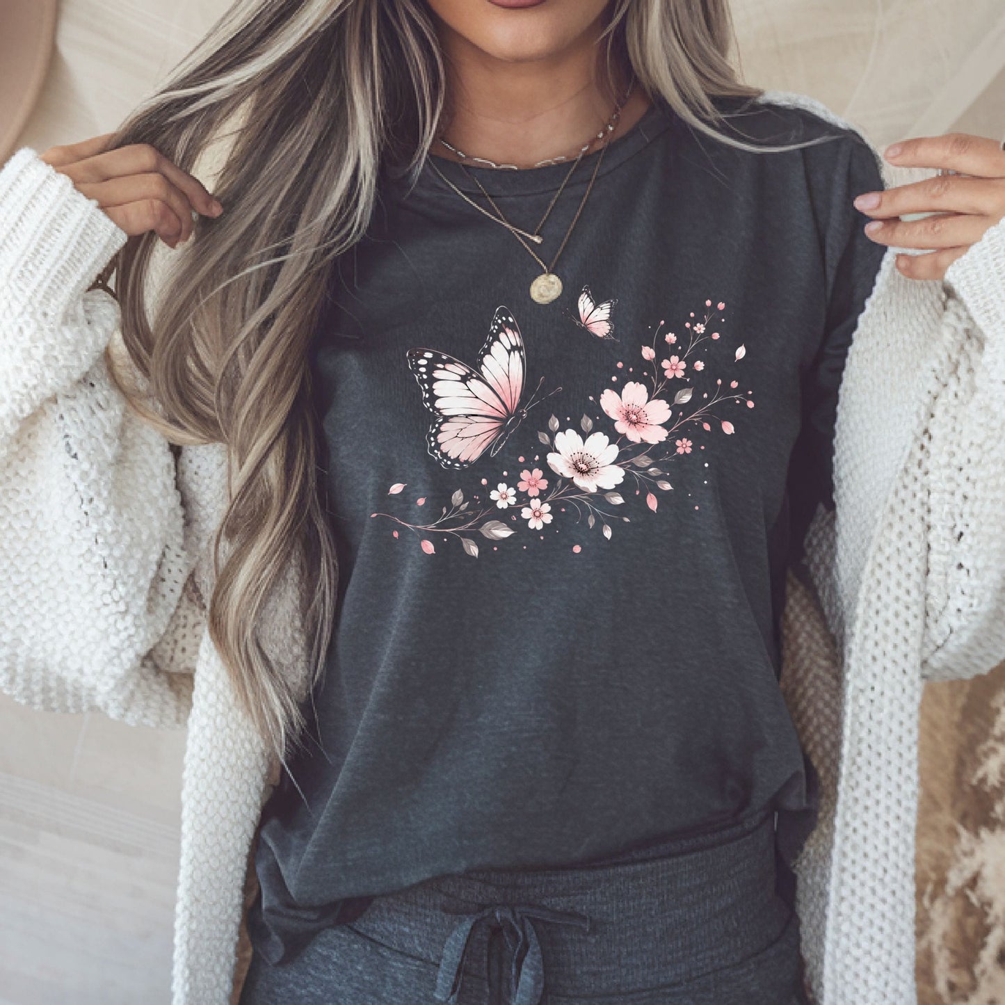 Person wearing a dark gray t-shirt with floral and butterfly design, holding a phone.