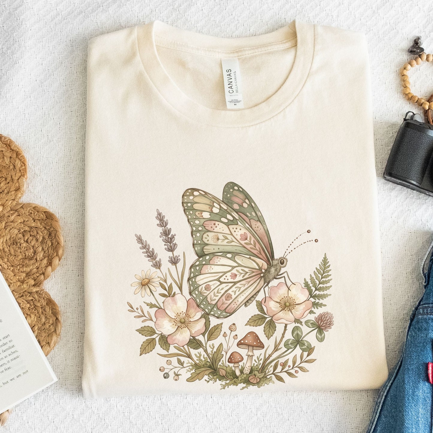 Beige t-shirt with a butterfly and floral design on a white surface.