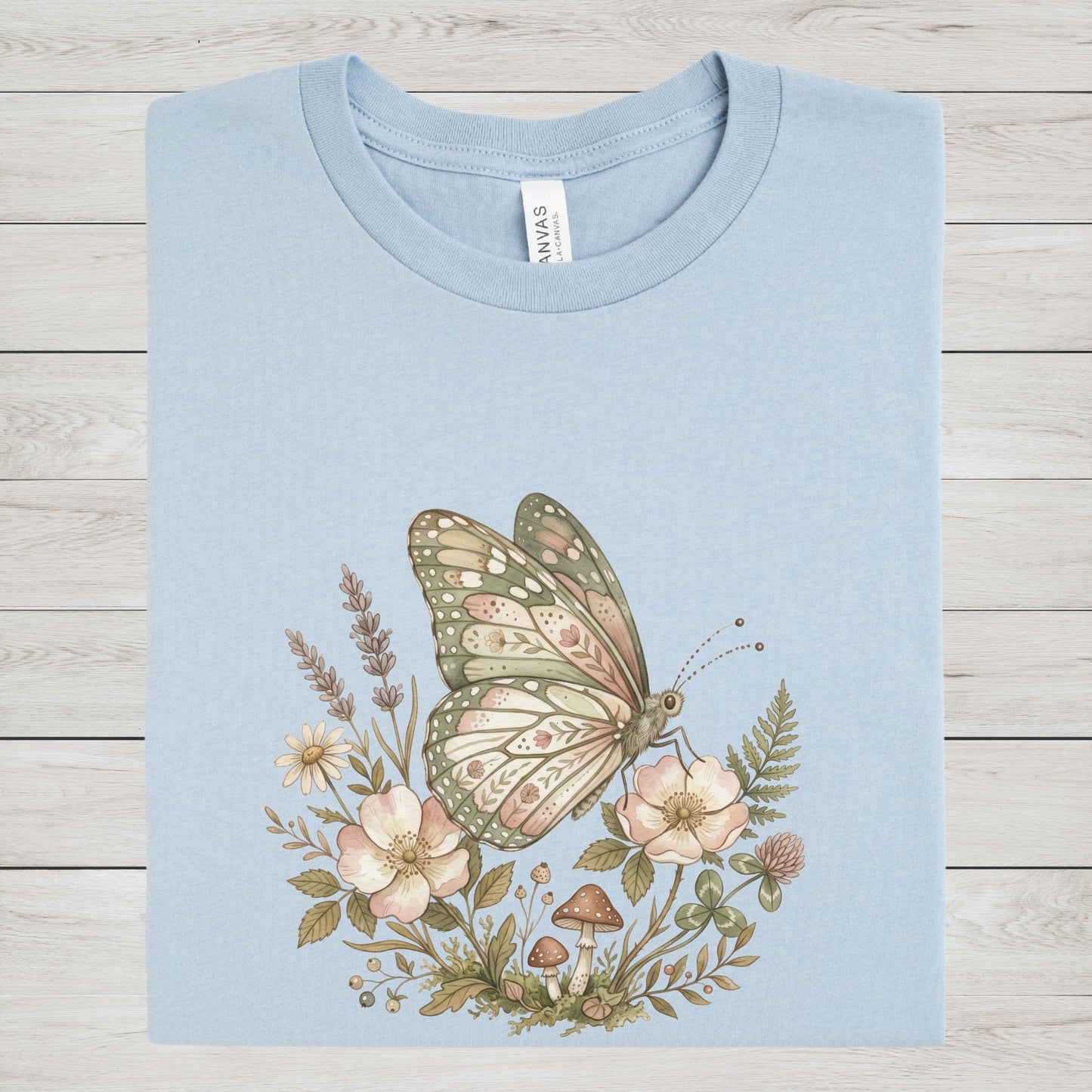 Light blue t-shirt with a butterfly and floral design on a wooden surface