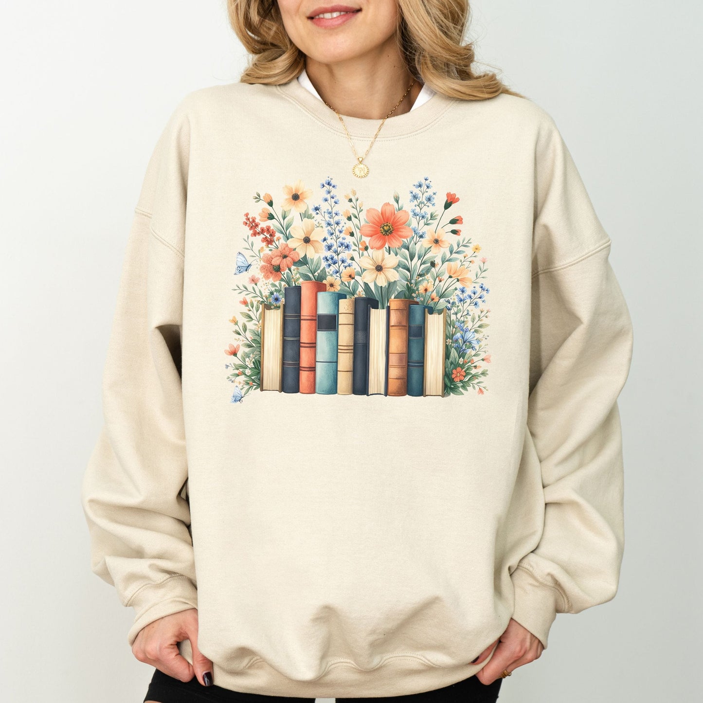 Beige sweatshirt with a floral and book design worn by a person on a plain background