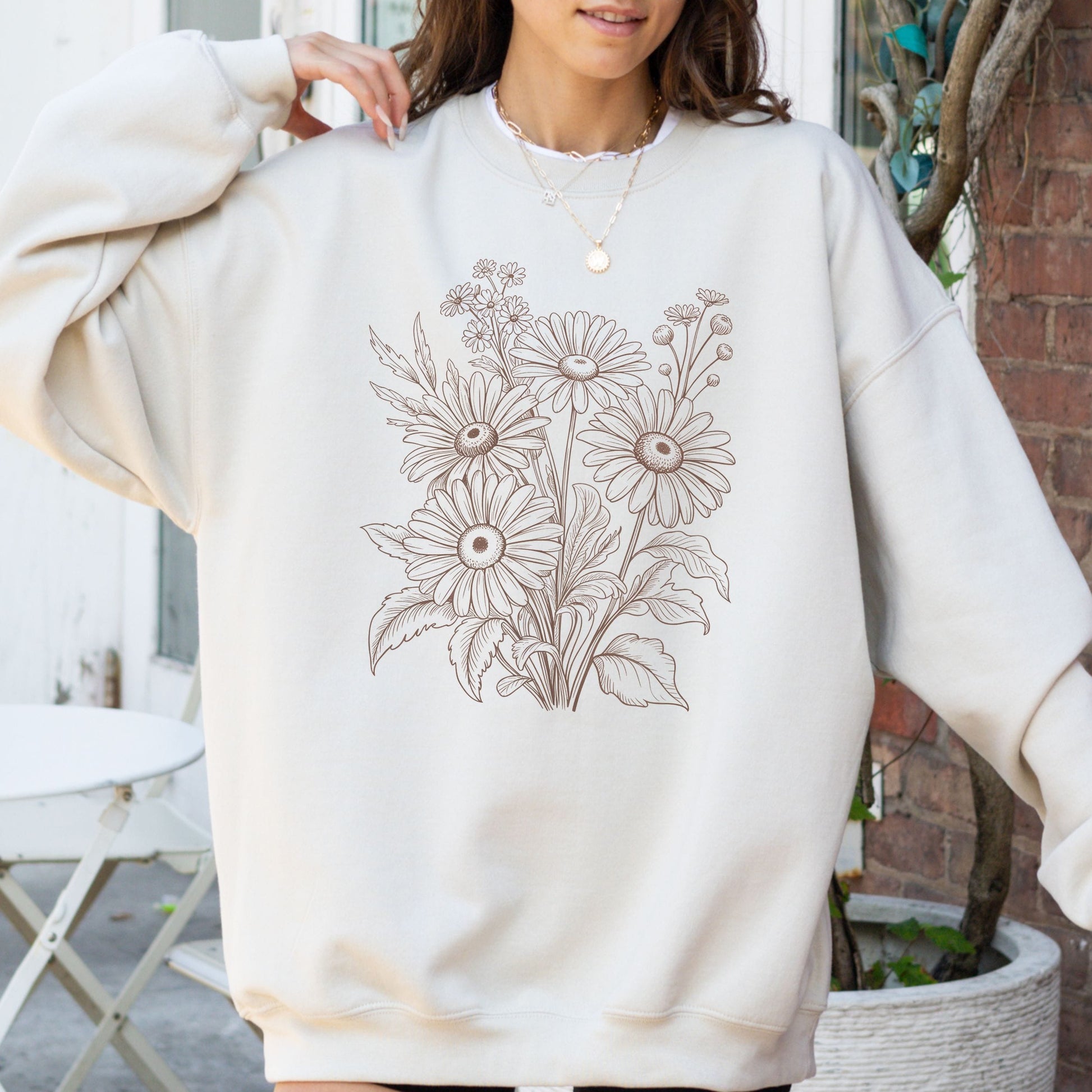 Person wearing a cream-colored sweatshirt with floral design outdoors.