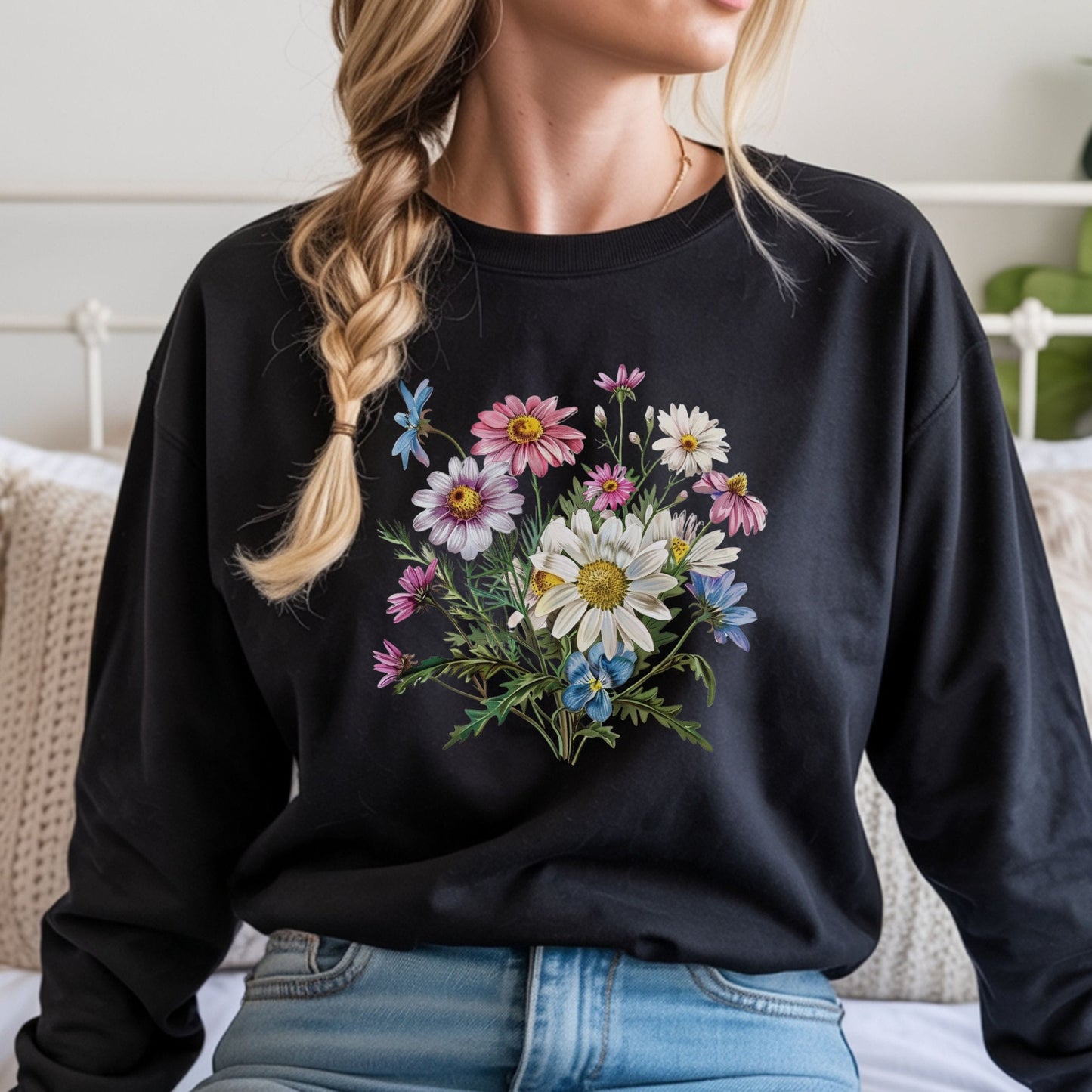 Person wearing a black long sleeve t-shirt with a floral design, sitting on a bed.