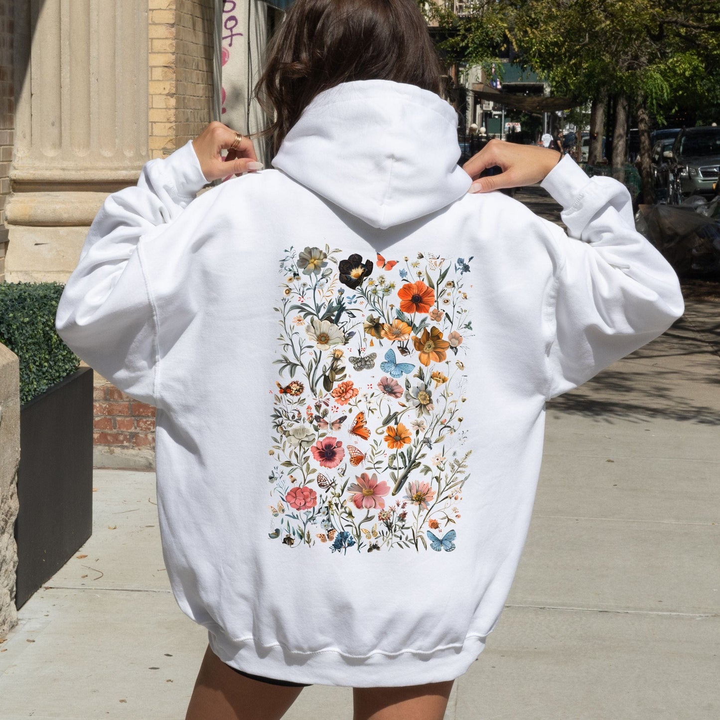 Person wearing a white hoodie with a colorful floral design on the back, standing outdoors.