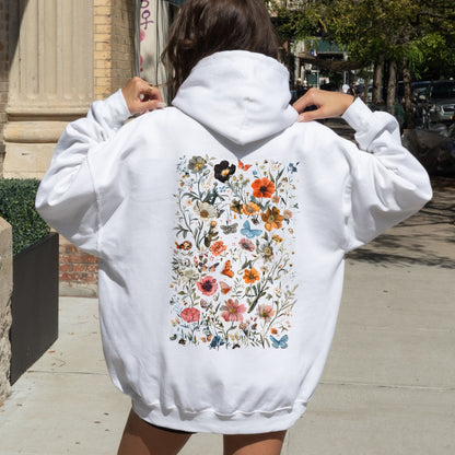Person wearing a white hoodie with a colorful floral design on the back, standing outdoors.