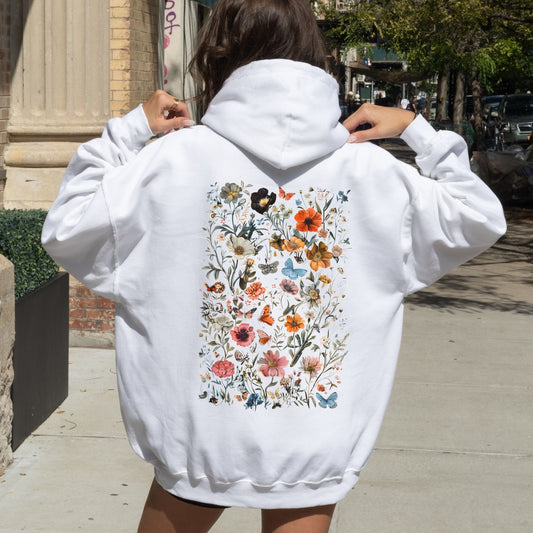 Person wearing a white hoodie with a colorful floral design on the back, standing outdoors.
