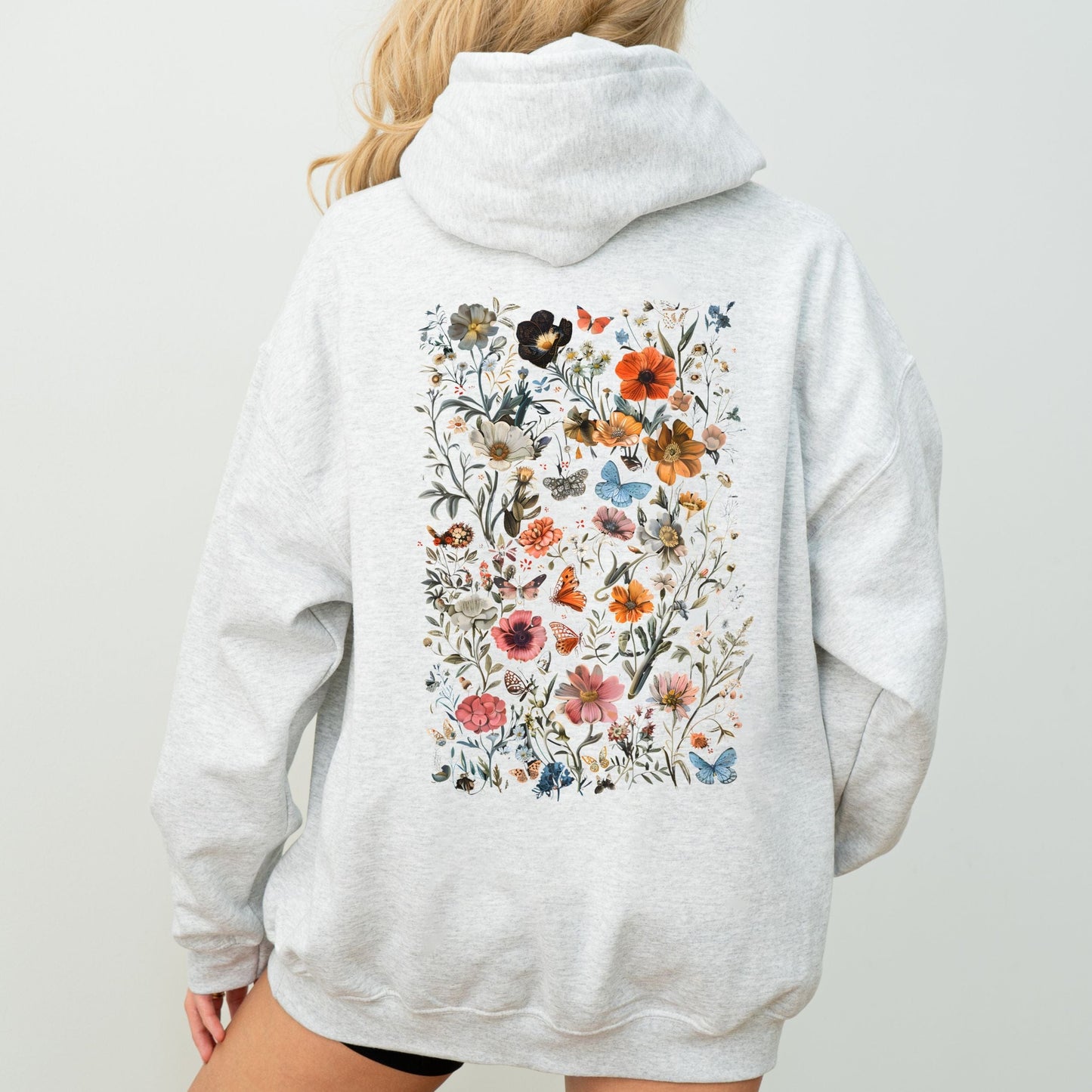Person wearing a gray hoodie with a colorful floral design on the back against a plain background