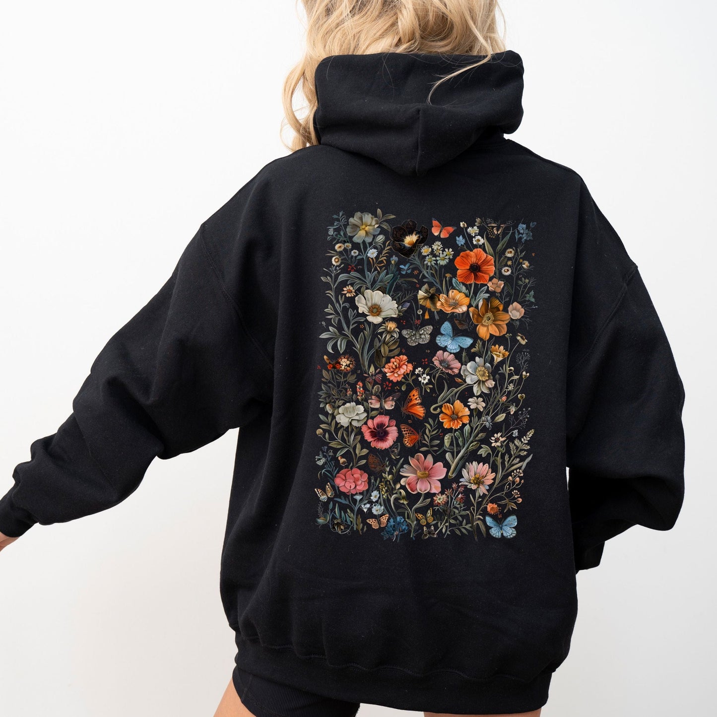 Person wearing a black hoodie with floral designs on the back against a white background