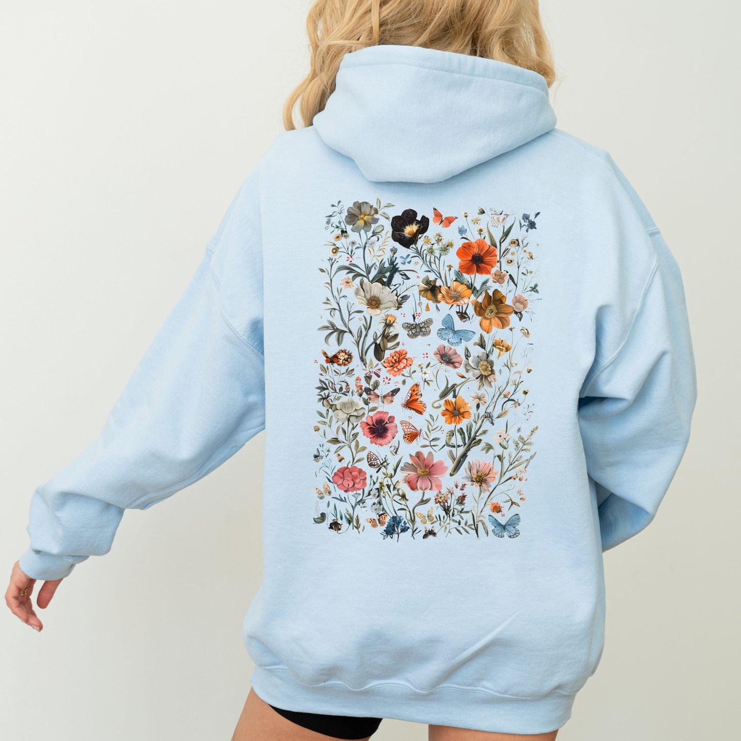 Light blue hoodie with floral design on the back worn by a person against a plain background