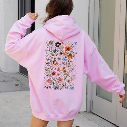 Person wearing a pink hoodie with a floral design on the back, standing in front of a door.
